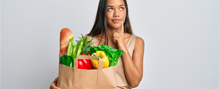 一名女子拿着装满健康食品的购物袋，看起来在思考