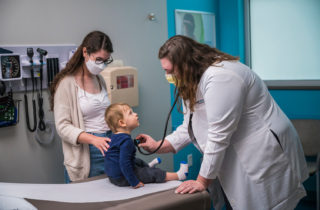 一名妇女和儿童访问OnCall紧急护理提供商。医生正在用听诊器检查孩子的心脏。