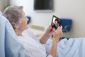 Senior female patient in hospital video chats with daughter on tablet.
